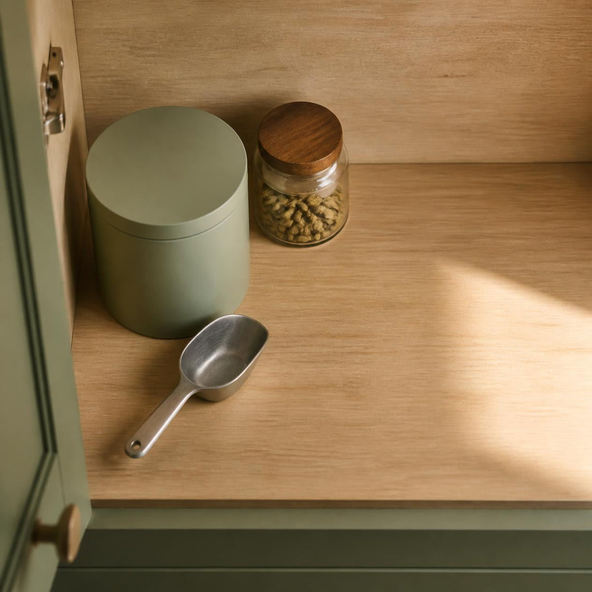 Sealed protein powder tub and dry steel scoop on a shelf inside a kitchen cupboard, away from heat and sunlight