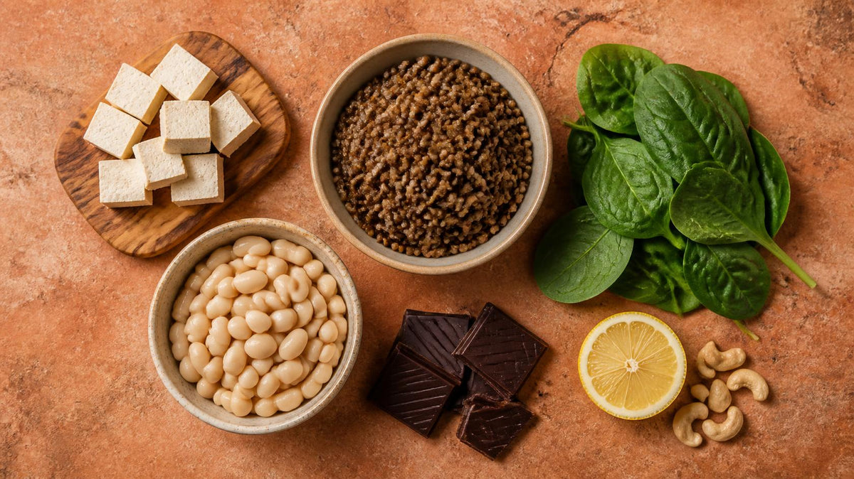 Flat lay of lentils, white beans, tofu, spinach, dark chocolate, lemon and cashews on a warm terracotta stone surface